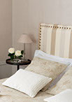 Tête de lit recouverte d'un tissu à rayures avec une finition cloutée, cache oreillers et dessus lit en tissu damassé coordonné.