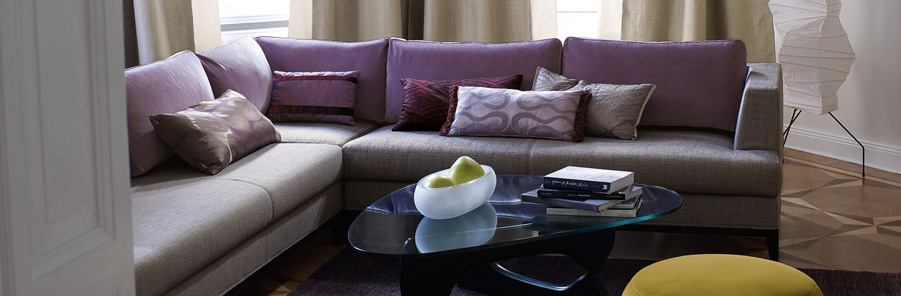 Canapé d'angle recouvert d'un tissu tramé gris pour le tour et l'assise et  pour les coussins de dos d'une toile violette.